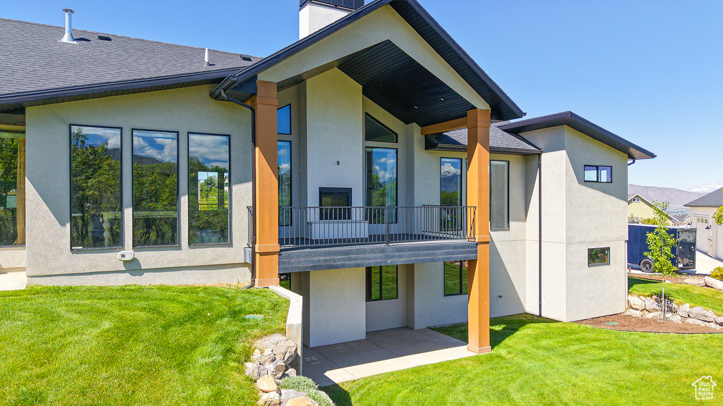 Rear view of house featuring stucco siding, a lawn, a patio, and a chimney