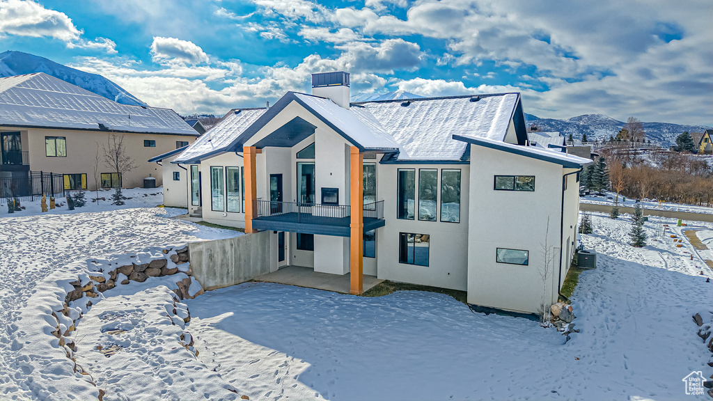 Snow covered back of property with a balcony and a mountain view