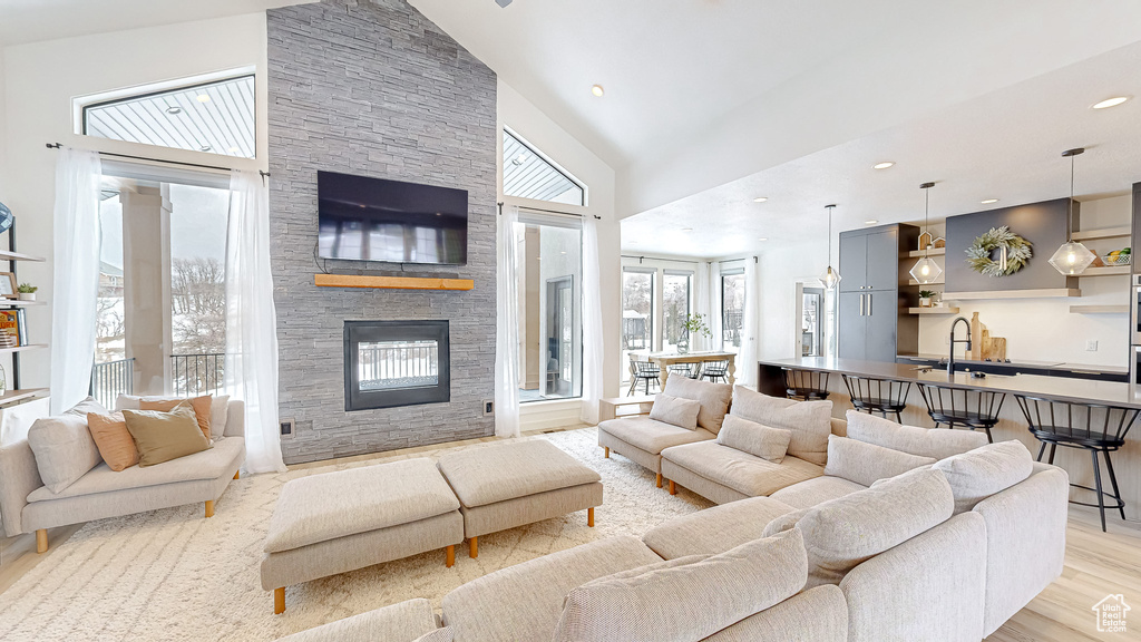 Living room featuring sink, high vaulted ceiling, light hardwood / wood-style flooring, and a stone fireplace