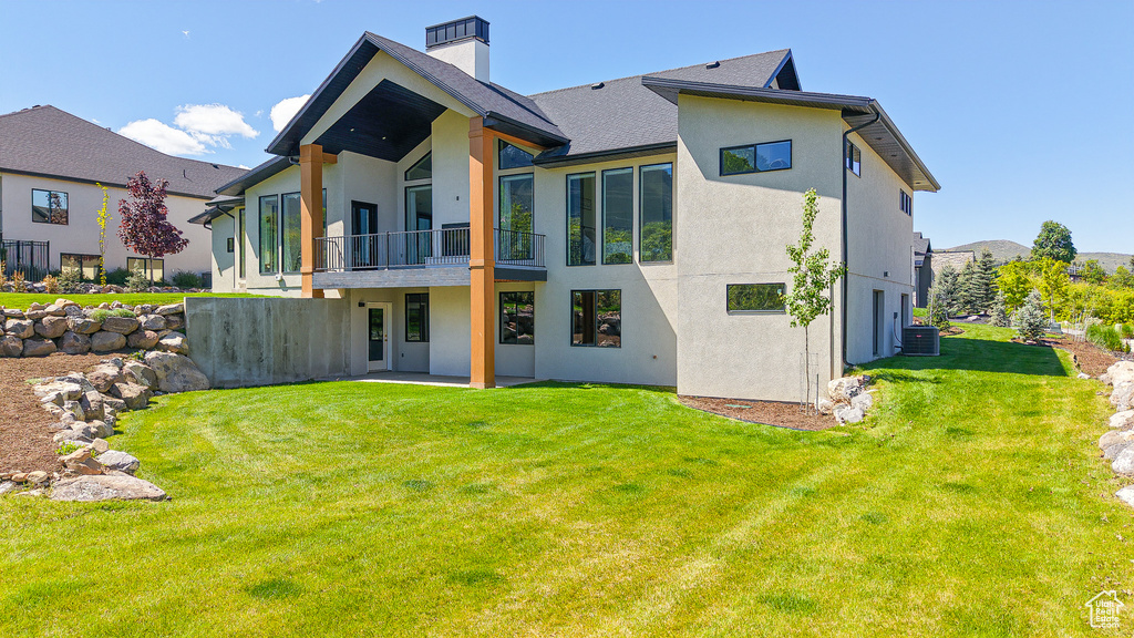 Back of property with a balcony, stucco siding, a yard, and a chimney