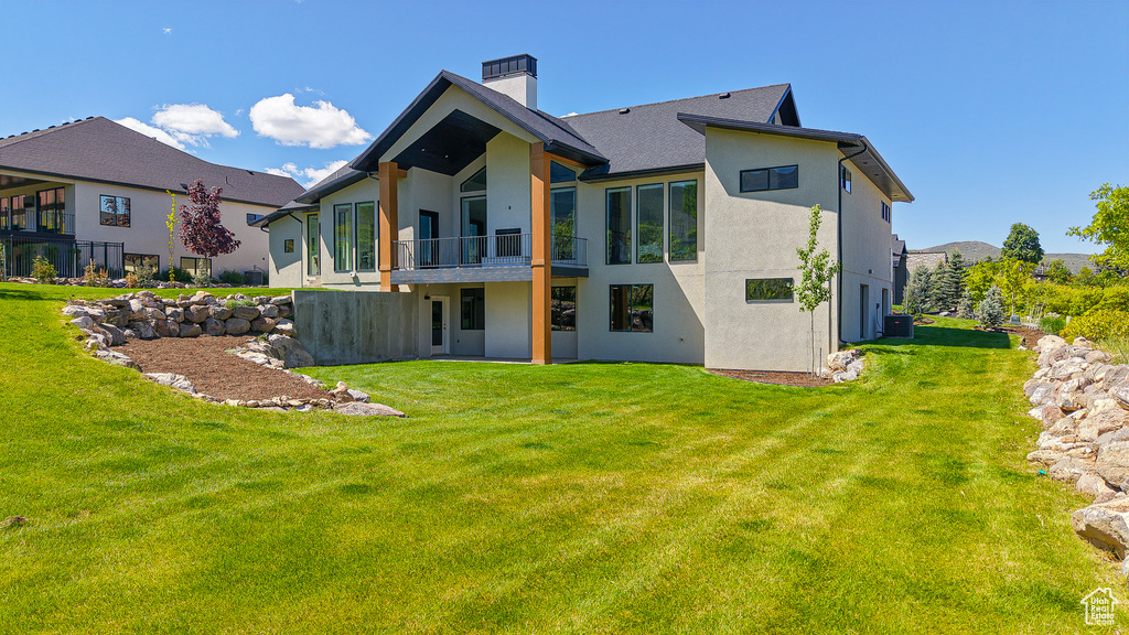 Rear view of house with a balcony, stucco siding, a chimney, and a lawn
