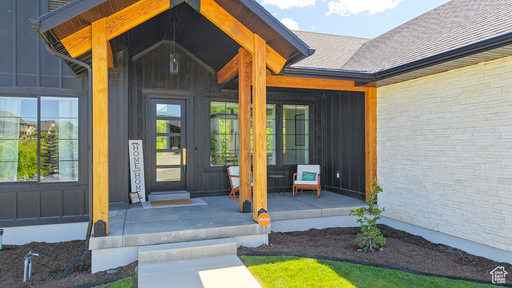 View of exterior entry with a porch, board and batten siding, and roof with shingles
