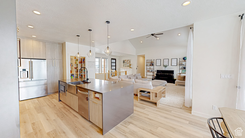 Kitchen with sink, built in appliances, decorative light fixtures, vaulted ceiling, and an island with sink