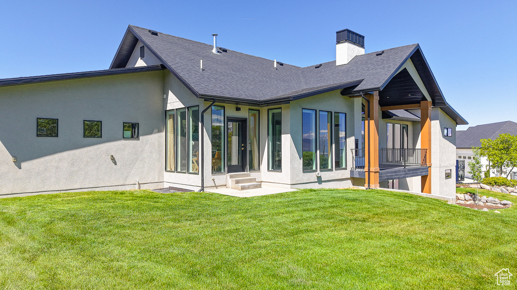 Rear view of property with stucco siding, a lawn, a shingled roof, and a chimney