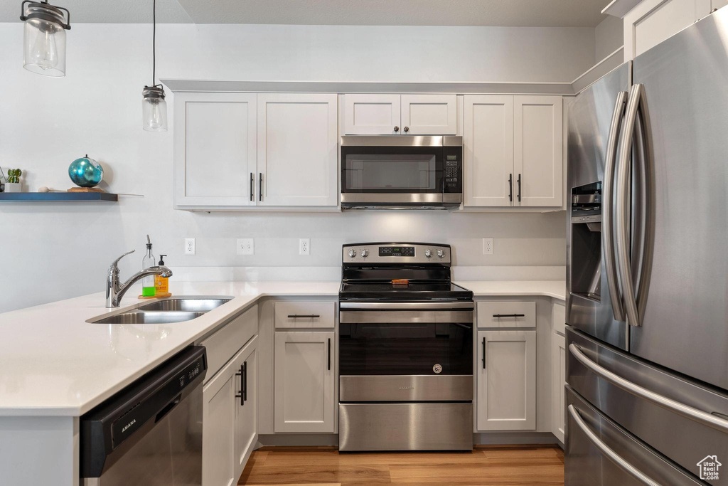Kitchen featuring stainless steel appliances, sink, pendant lighting, light hardwood / wood-style flooring, and white cabinetry