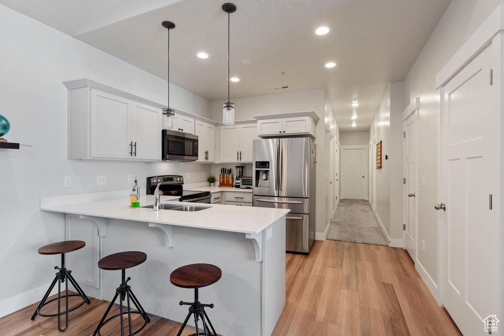 Kitchen featuring white cabinets, appliances with stainless steel finishes, kitchen peninsula, and pendant lighting