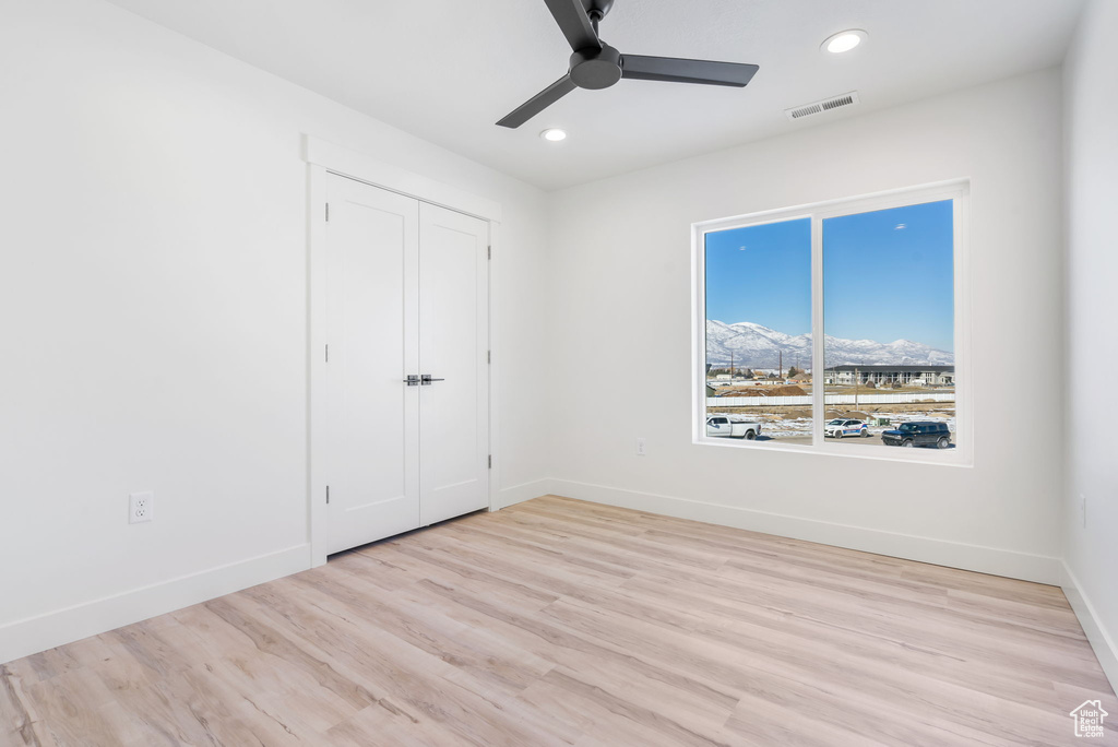 Unfurnished bedroom with ceiling fan, light wood-type flooring, a closet, and a mountain view