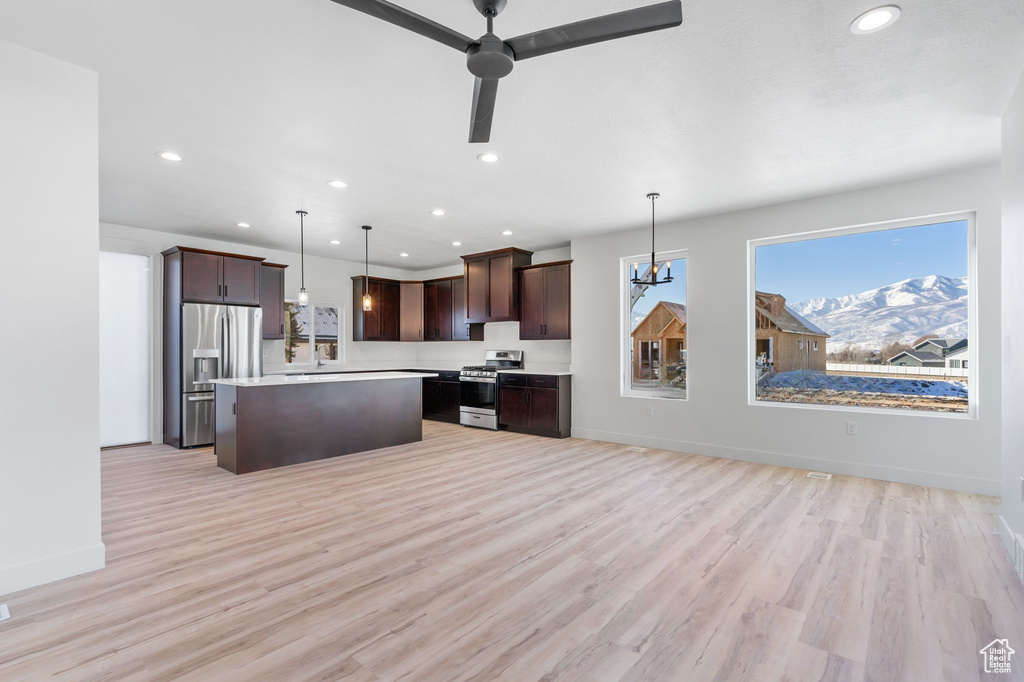 Kitchen featuring light wood-type flooring, appliances with stainless steel finishes, dark brown cabinetry, and hanging light fixtures