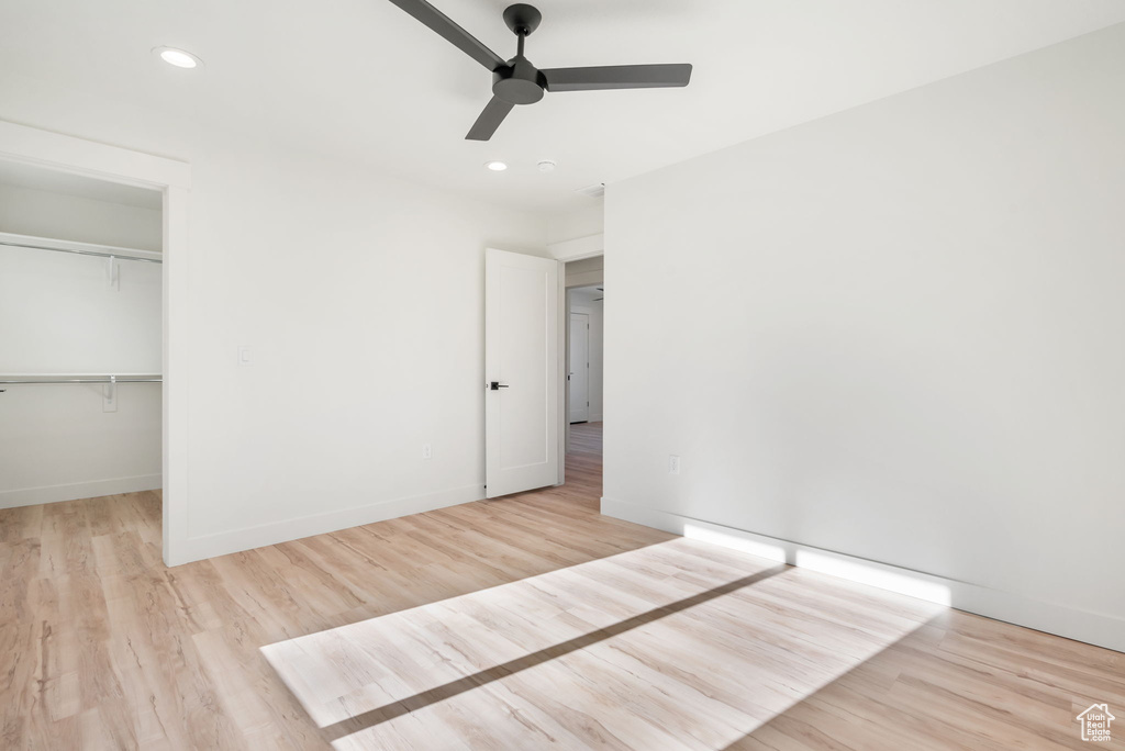 Unfurnished bedroom with a walk in closet, a closet, ceiling fan, and light hardwood / wood-style flooring