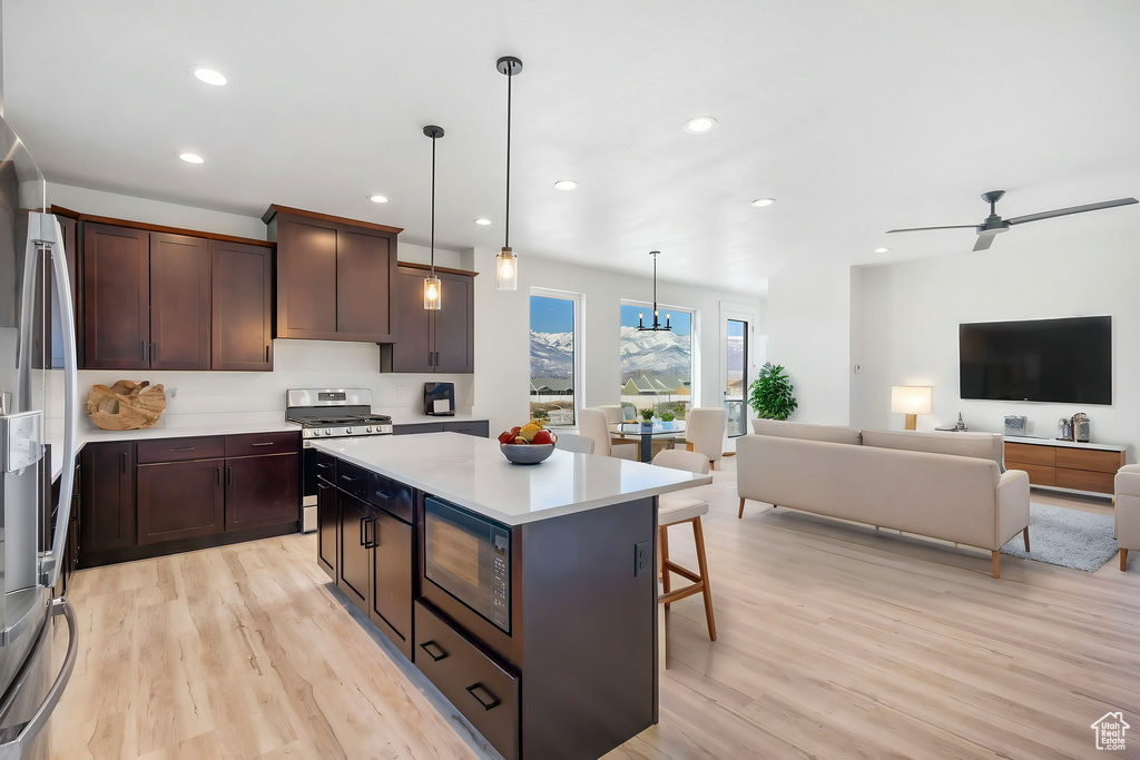 Kitchen featuring light hardwood / wood-style floors, black microwave, stainless steel gas stove, hanging light fixtures, and a center island