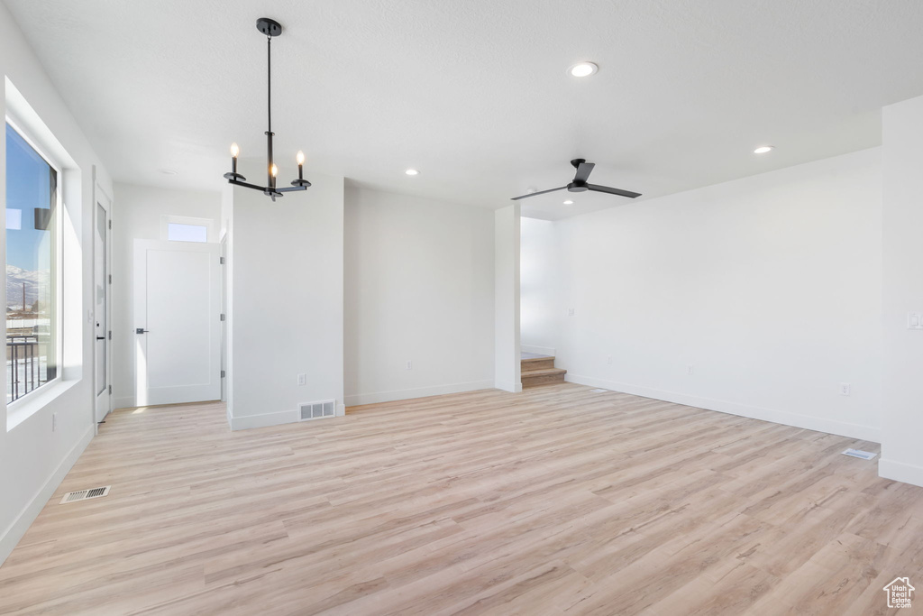 Spare room featuring ceiling fan with notable chandelier and light hardwood / wood-style floors