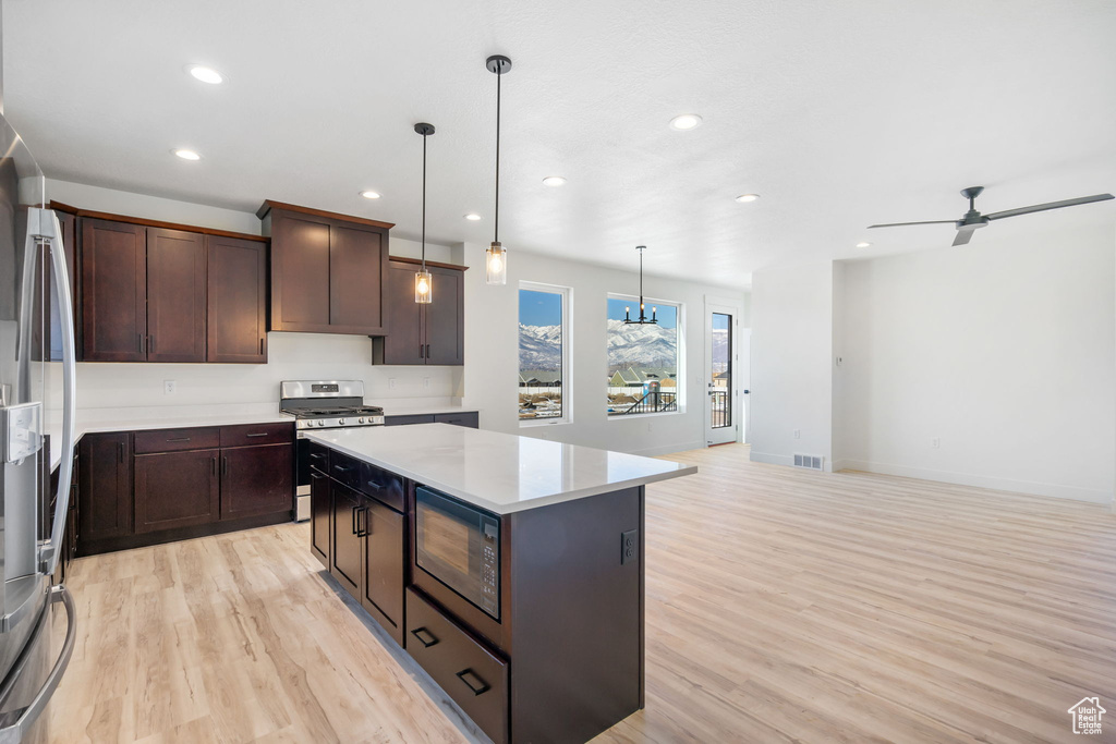 Kitchen featuring stainless steel appliances, decorative light fixtures, ceiling fan, light hardwood / wood-style floors, and a kitchen island