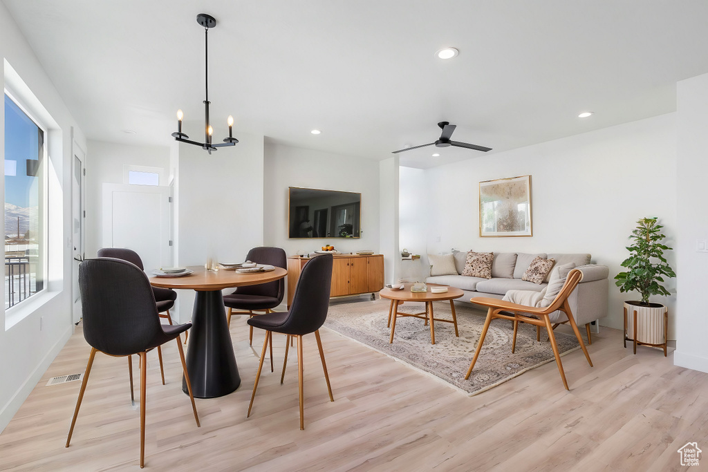 Dining space with ceiling fan with notable chandelier and light hardwood / wood-style flooring