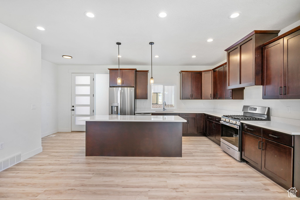 Kitchen with light hardwood / wood-style flooring, decorative light fixtures, a kitchen island, appliances with stainless steel finishes, and sink