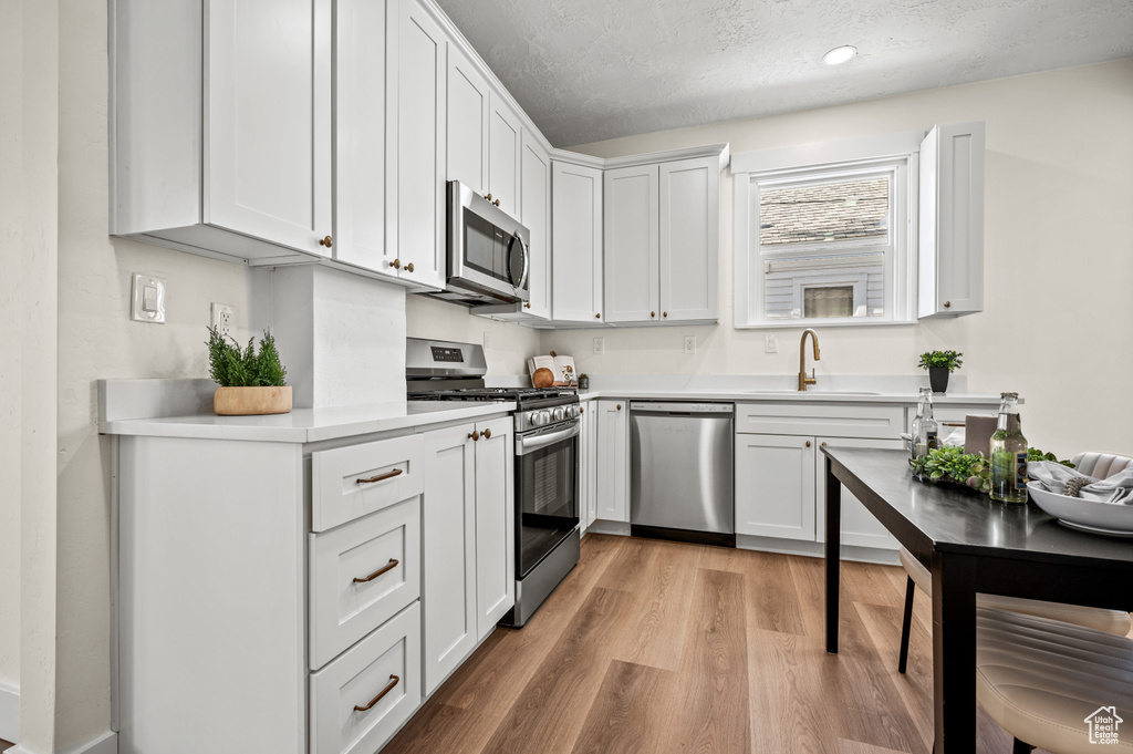 Kitchen featuring stainless steel appliances, light countertops, light wood-style flooring, a textured ceiling, and white cabinets