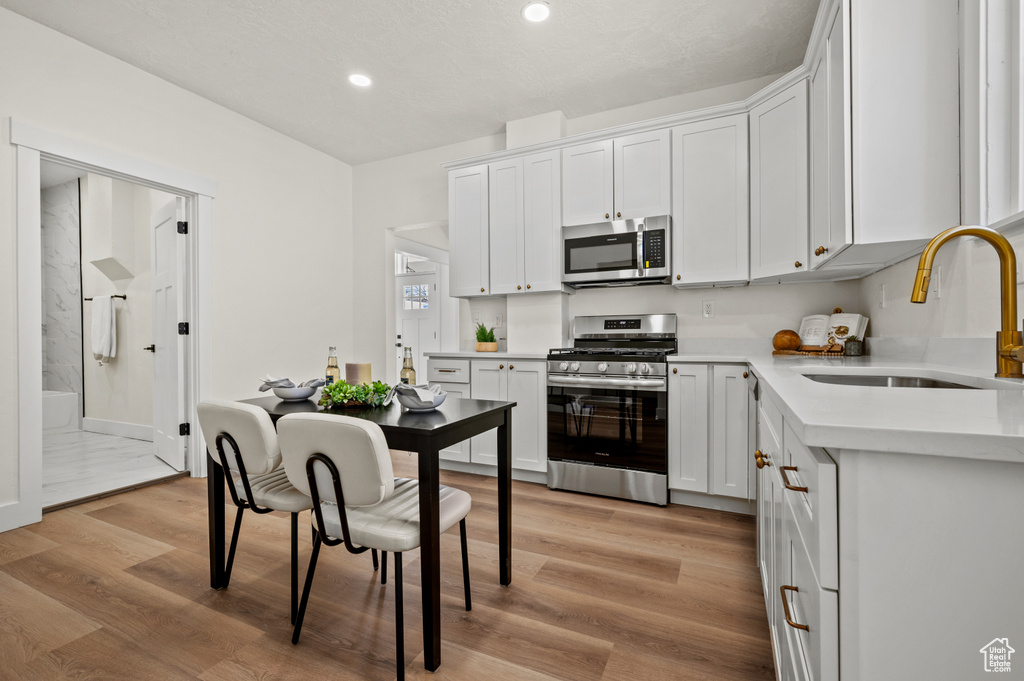 Kitchen with appliances with stainless steel finishes, light wood-style flooring, recessed lighting, light countertops, and white cabinetry