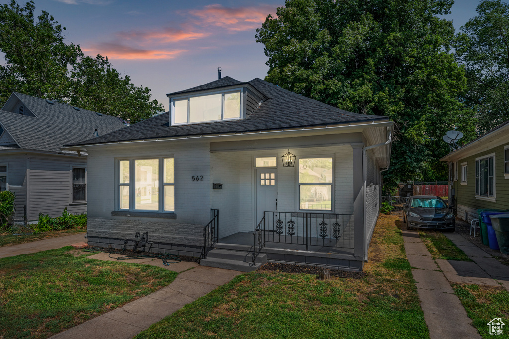 Bungalow featuring covered porch, roof with shingles, a front lawn, and brick siding