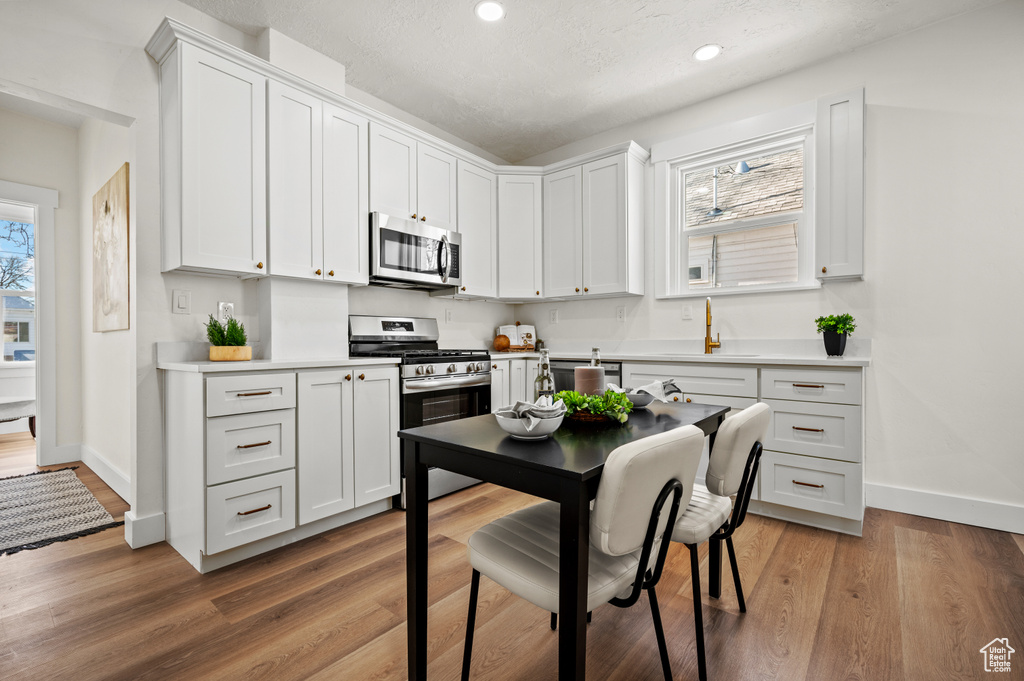 Kitchen featuring stainless steel appliances, recessed lighting, light countertops, light wood-type flooring, and white cabinetry