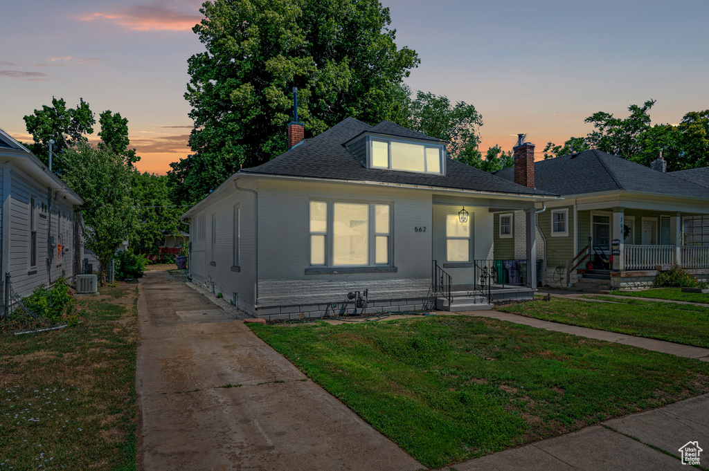 Bungalow-style home featuring a chimney, driveway, covered porch, and a front lawn