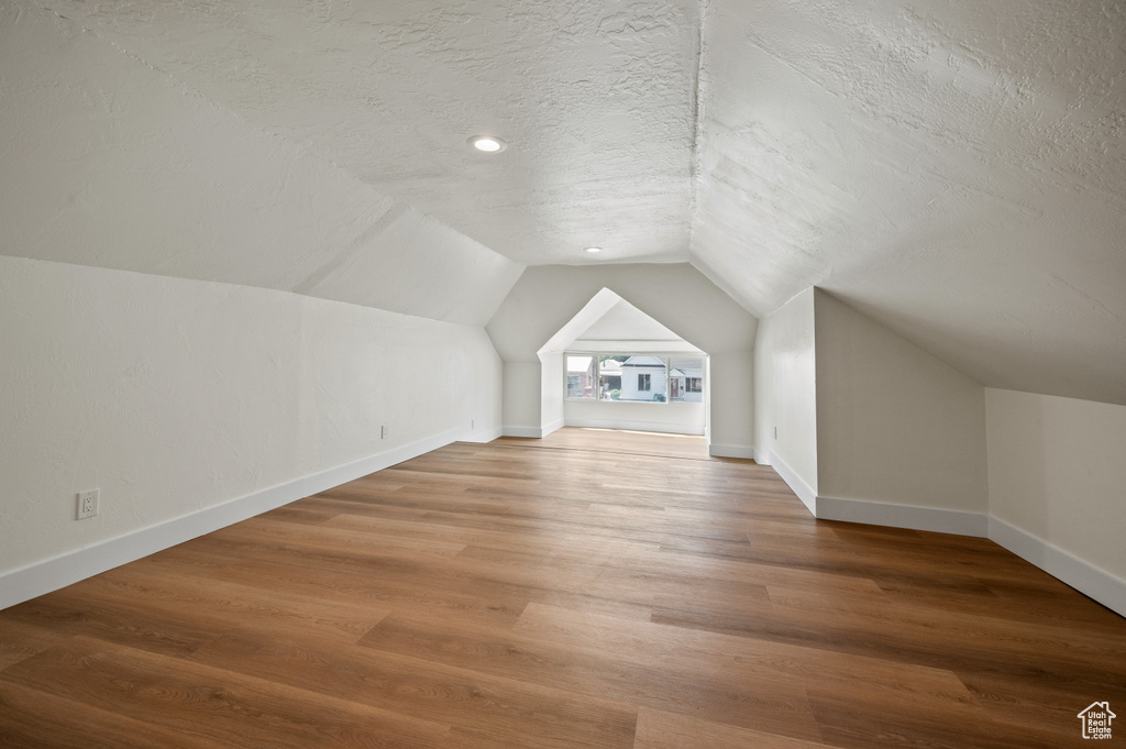 Additional living space featuring a textured ceiling, vaulted ceiling, and wood finished floors