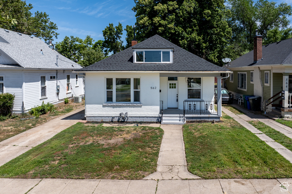 Bungalow-style home with covered porch, roof with shingles, a front lawn, brick siding, and a chimney