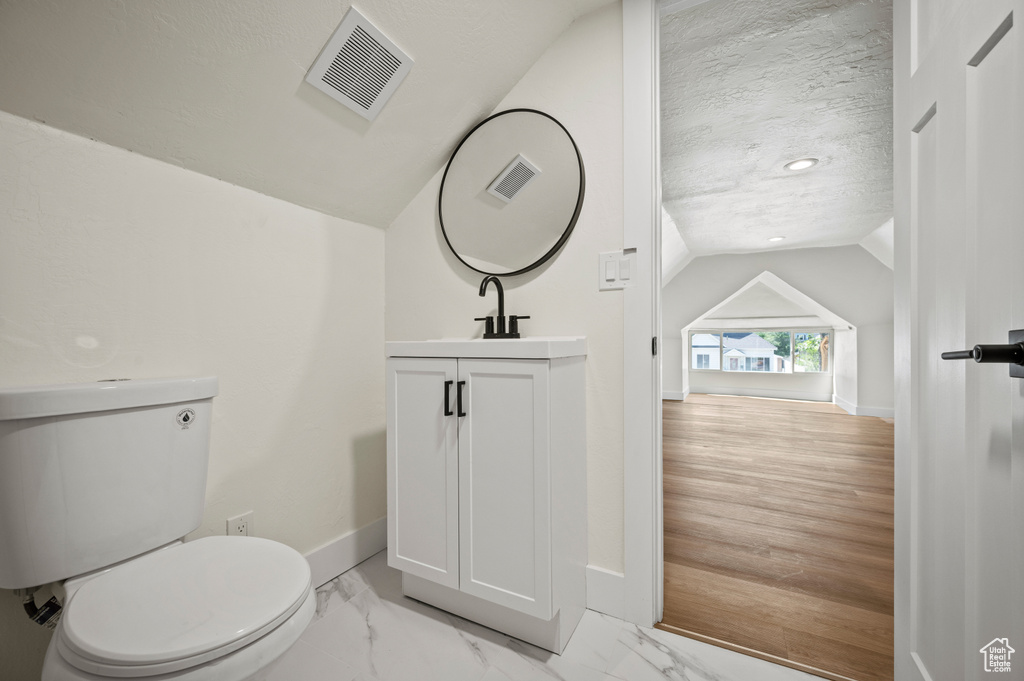 Half bathroom with vaulted ceiling, vanity, marble finish floors, and a textured ceiling