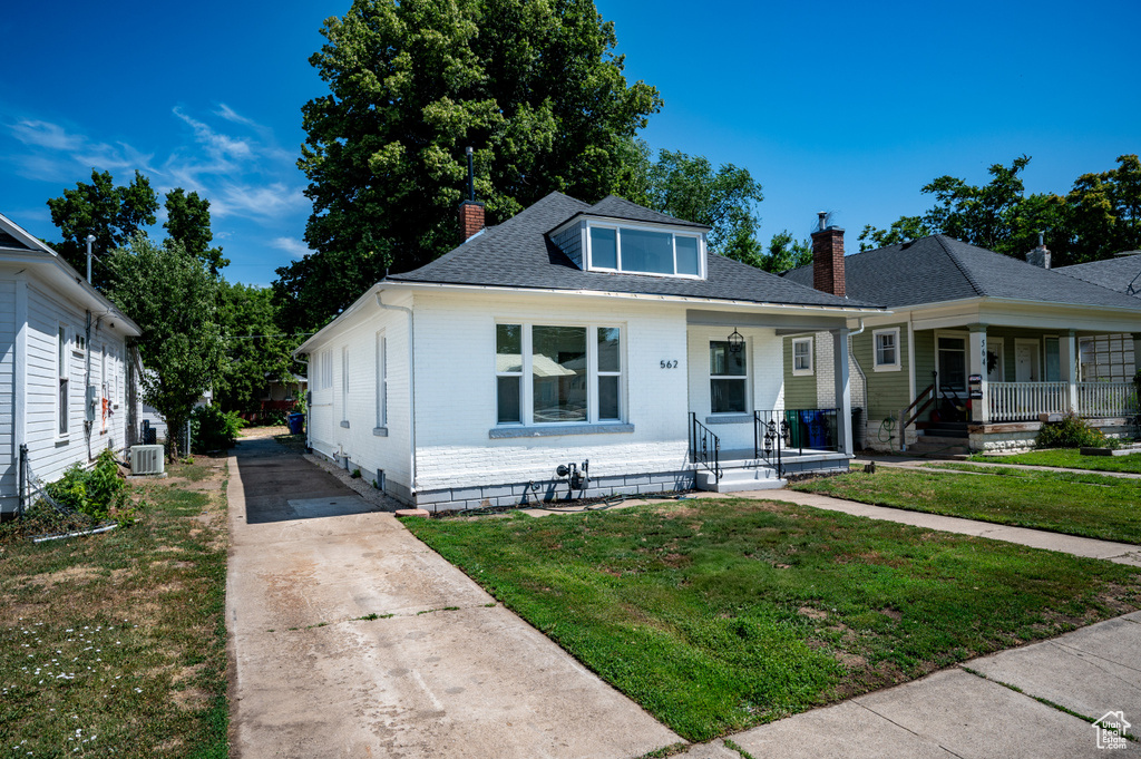 Bungalow featuring a chimney, covered porch, driveway, and a front yard