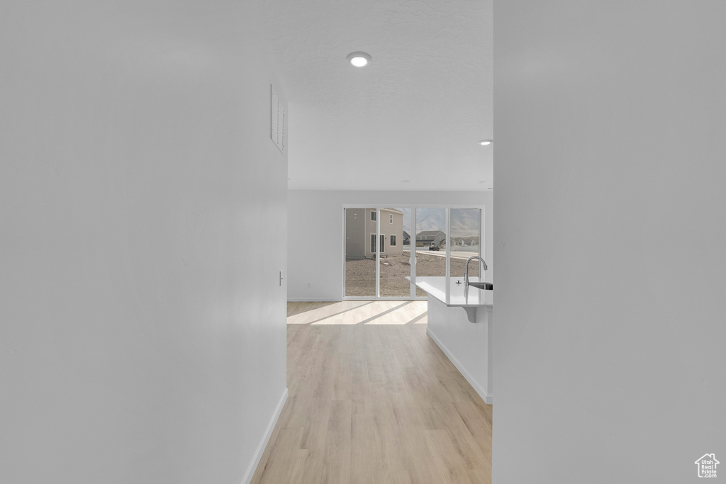 Hallway with baseboards, light wood finished floors, a sink, and recessed lighting