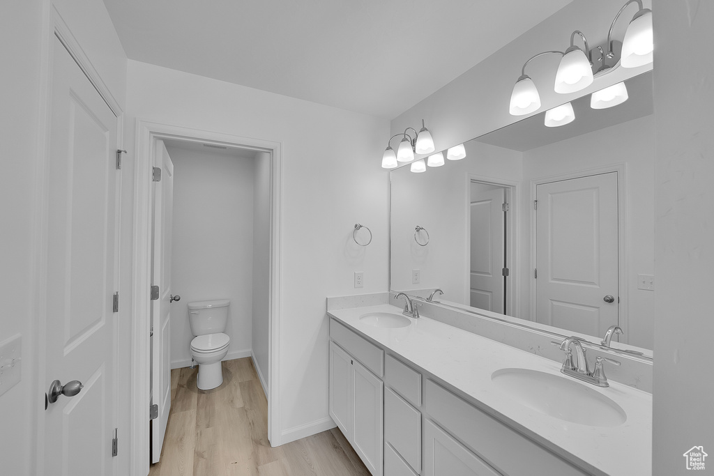 Full bathroom with double vanity, wood finished floors, toilet, and baseboards