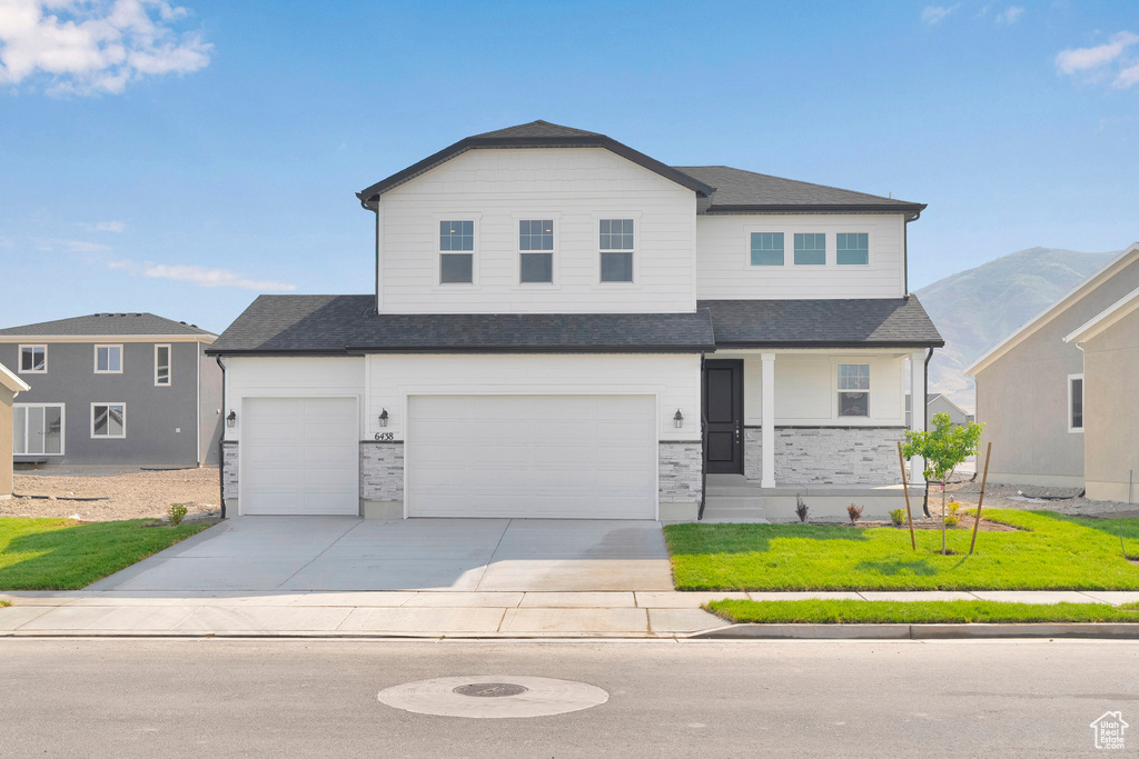 View of front of house with an attached garage, concrete driveway, a front lawn, and a shingled roof