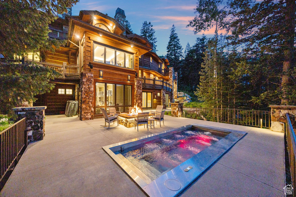 Rear view of house with an in-ground hot tub, a balcony, a fire pit, and a patio area