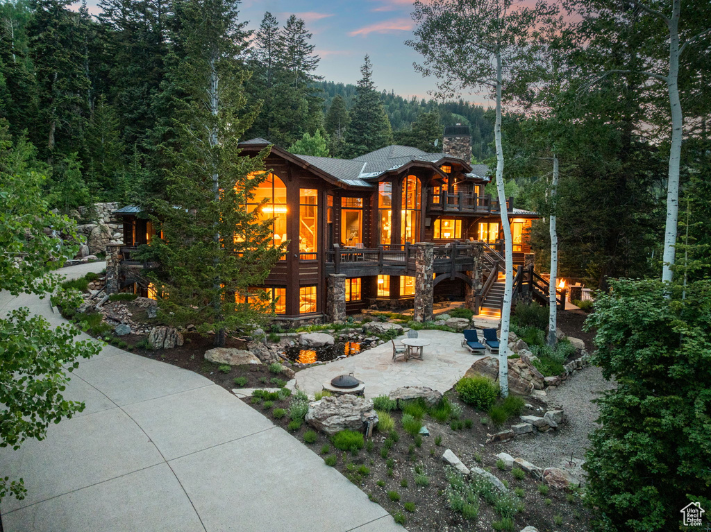 Back of property at dusk with a patio, a chimney, stairway, stone siding, and a balcony