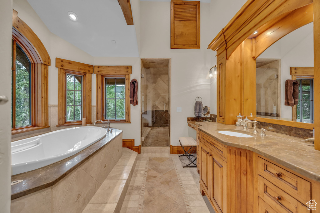 Bathroom with tiled shower, a garden tub, vanity, inlaid floor details, and lofted ceiling