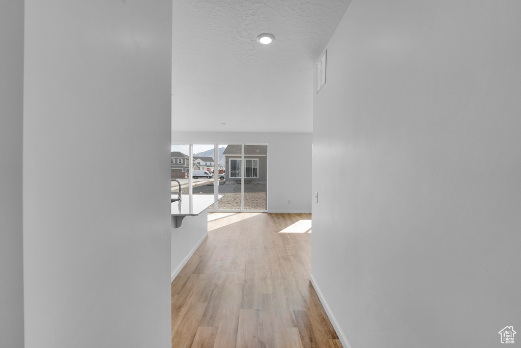 Hall featuring baseboards, light wood-type flooring, and a textured ceiling