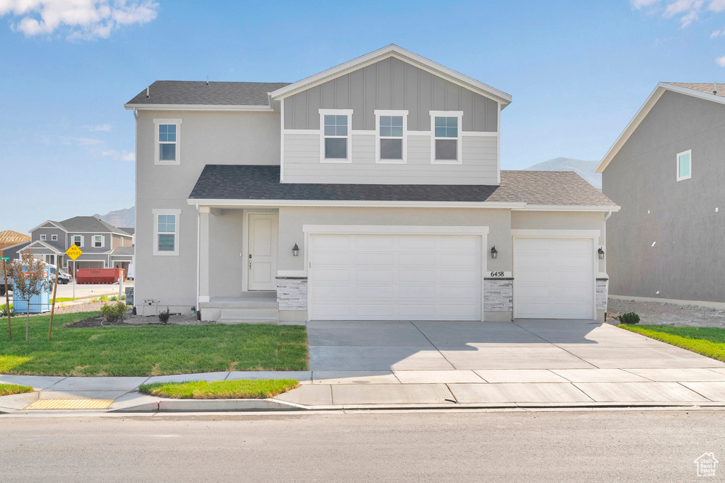 View of front of property with driveway, stone siding, a front yard, and board and batten siding