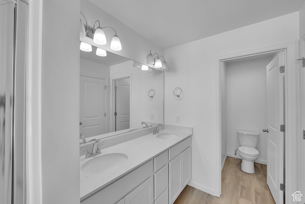 Full bath with double vanity, wood finished floors, and toilet