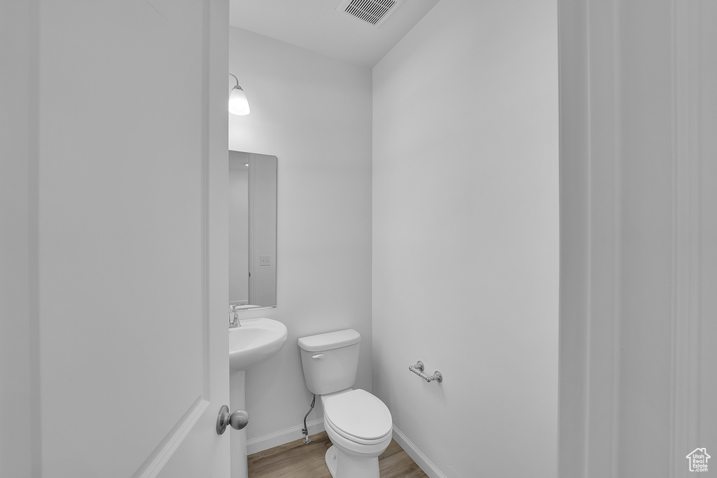 Half bath with wood finished floors, toilet, baseboards, and a sink