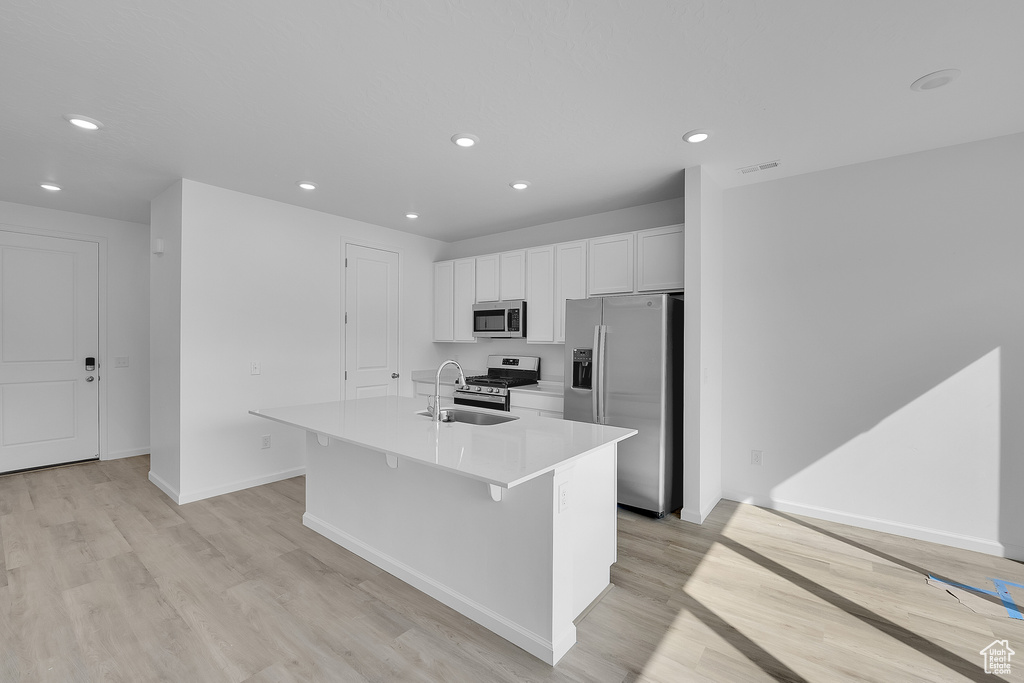Kitchen featuring appliances with stainless steel finishes, a sink, a center island with sink, light wood-type flooring, and recessed lighting