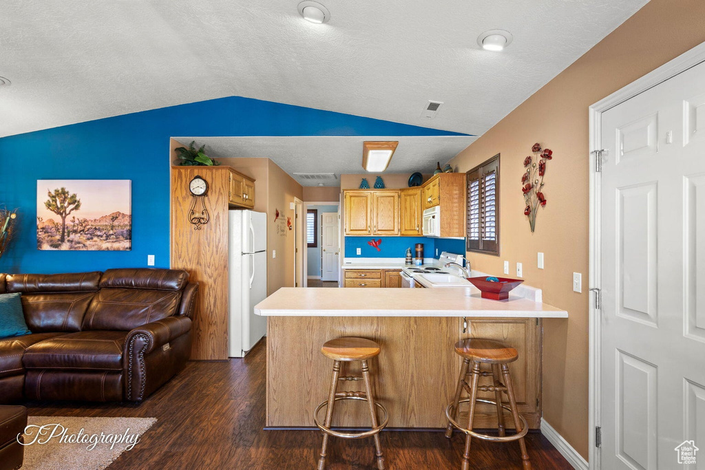 Kitchen with white appliances, kitchen peninsula, vaulted ceiling, dark hardwood / wood-style floors, and a breakfast bar