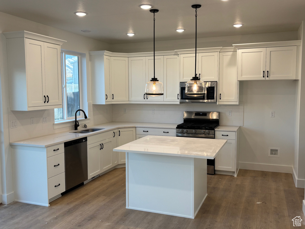 Kitchen with sink, white cabinets, hanging light fixtures, and appliances with stainless steel finishes