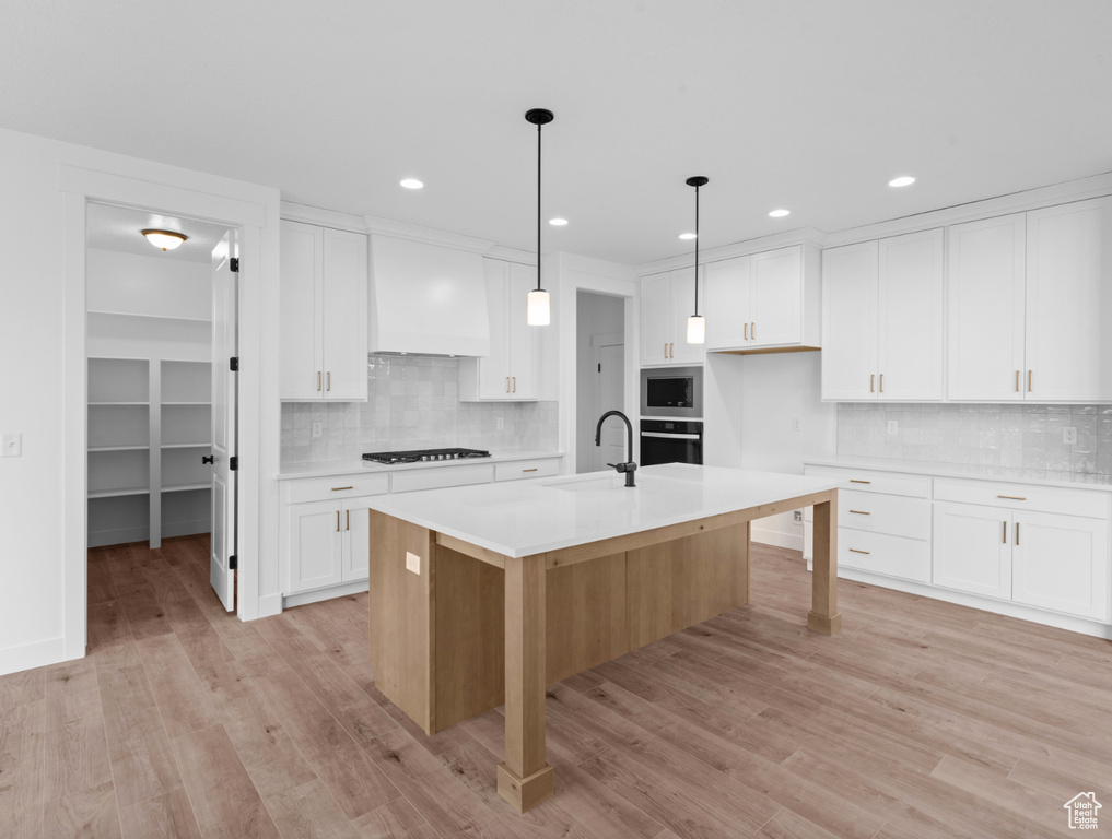 Kitchen featuring custom exhaust hood, black appliances, a sink, and backsplash