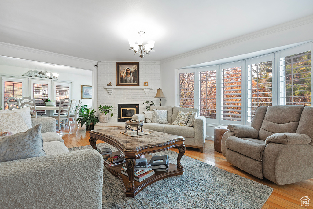 Living room with crown molding, light wood-type flooring, a fireplace, and a chandelier