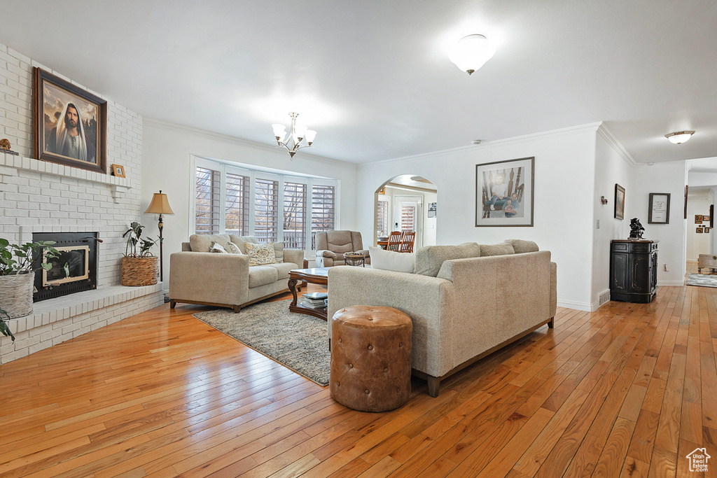 Living room featuring a chandelier, wood-type flooring, ornamental molding, and a brick fireplace