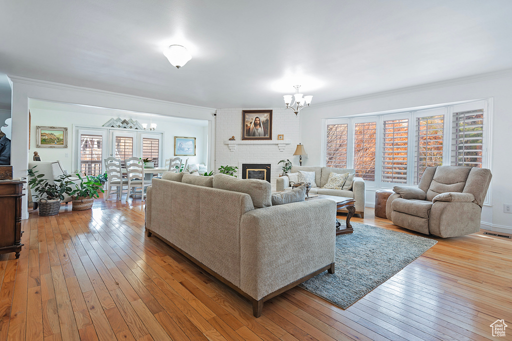 Living room featuring a notable chandelier, ornamental molding, a fireplace, and light hardwood / wood-style flooring