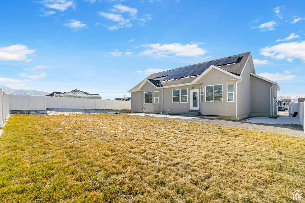 Back of house with solar panels, a patio, and a lawn