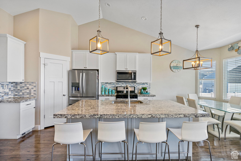 Kitchen with stainless steel appliances, decorative light fixtures, white cabinetry, and backsplash