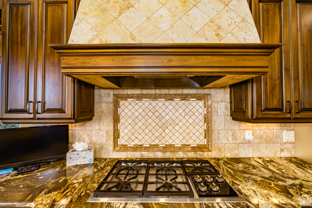 Kitchen with stainless steel gas cooktop, dark stone countertops, custom exhaust hood, and decorative backsplash