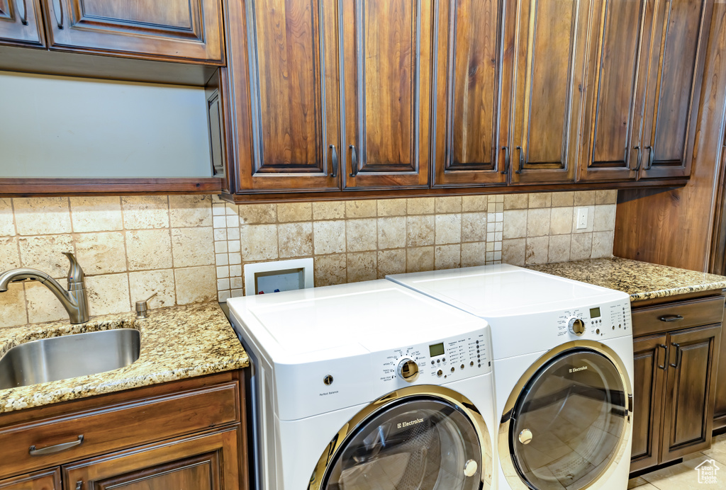 Laundry area with sink, washing machine and clothes dryer, light tile patterned floors, and cabinets