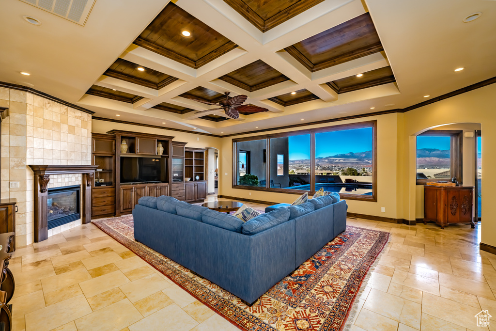 Living room with coffered ceiling, ornamental molding, ceiling fan, a fireplace, and beam ceiling
