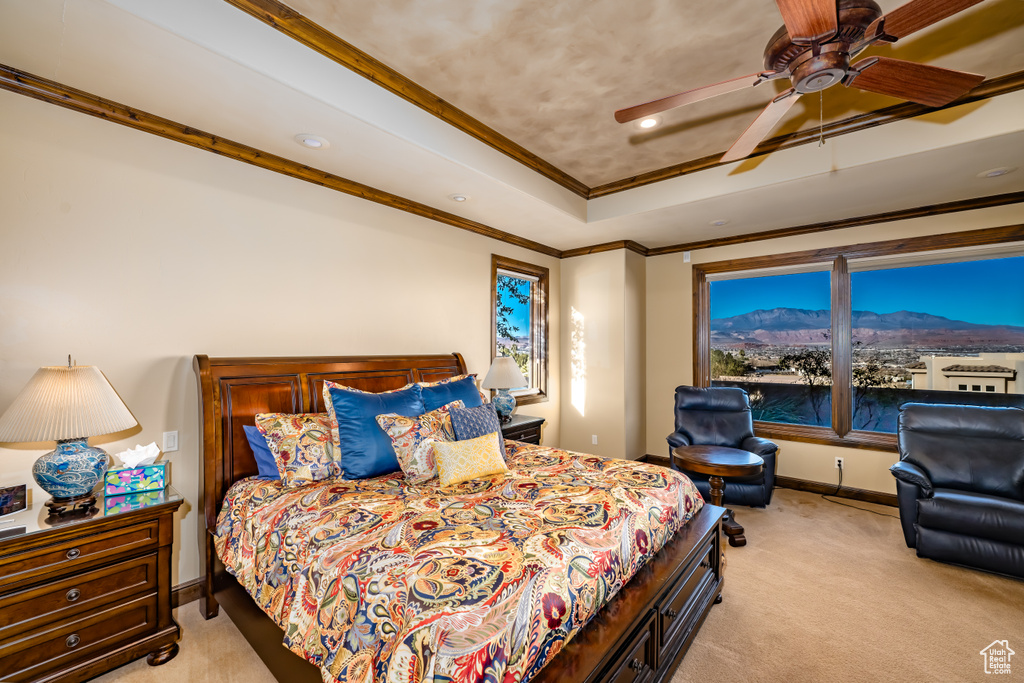 Carpeted bedroom featuring ceiling fan, crown molding, and a tray ceiling